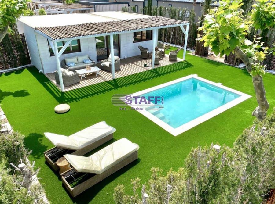 Piscina con encanto en jardín con césped Piscina pequeña en un jardín con césped, equipada con tumbonas y una pérgola de madera que crea un espacio acogedor al aire libre.